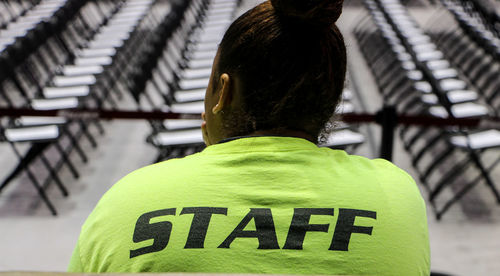 Rear view of woman in uniform with text against arranged chairs at stadium