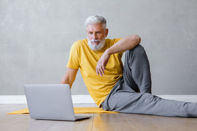 Mature man using laptop sitting on ground at home