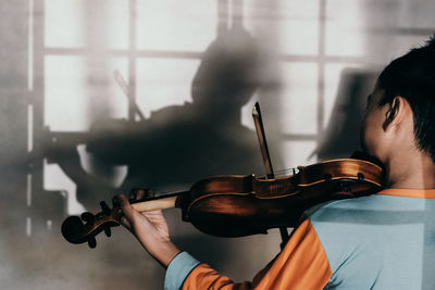 Rear view of boy playing violin against wall