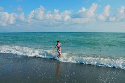 Woman wearing bikini while standing on shore at beach against sky