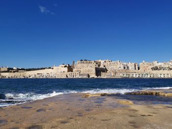 Buildings by sea against blue sky