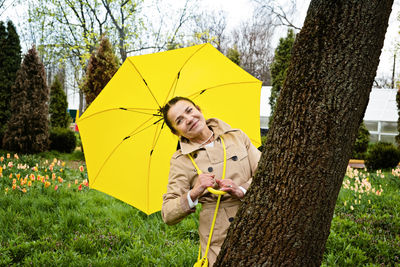Happy senior woman in yellow rain coat with yellow umbrella walking in park. cheerful mature