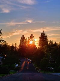 Road by trees against sky during sunset