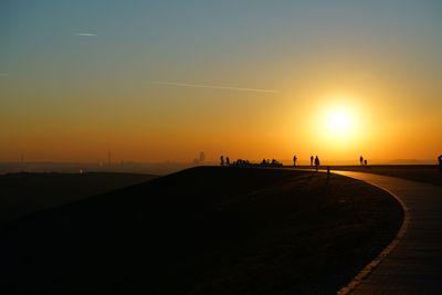Silhouette people on road against sky during sunset