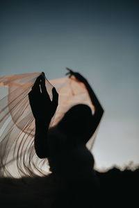 Silhouette woman with scarf against sky at sunset