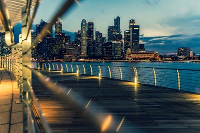 Illuminated buildings by river against sky in city