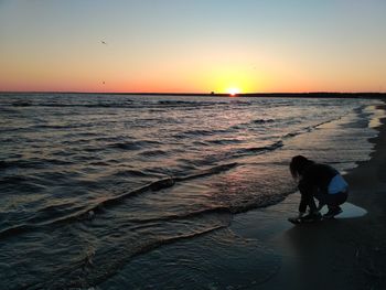 Silhouette man standing on beach against clear sky during sunset