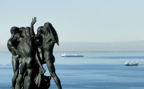 Human statues by sea against sky