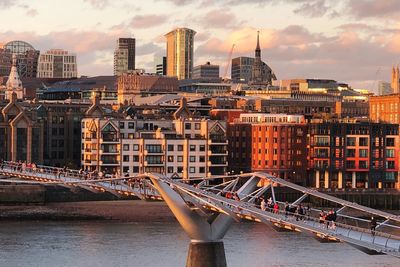 Bridge over river against buildings in city at sunset