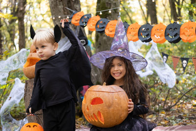 Two kids girl and boy in halloween costume with pumpkins in halloween decorations outdoor