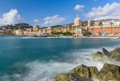 Buildings at waterfront against cloudy sky