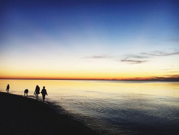 Silhouette people on beach against sky during sunset