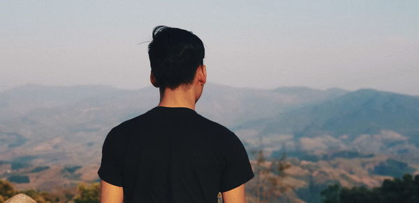 Rear view of man looking at mountains against sky