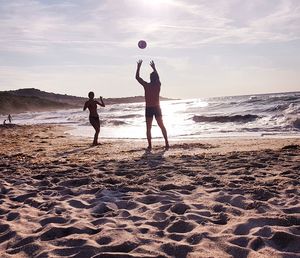 Men playing with ball on beach against sky