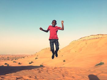Portrait of boy jumping over sand against sky