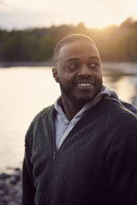 Smiling mid adult man looking away against lake during sunset