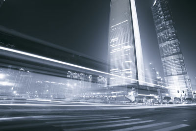 Illuminated road by buildings against sky in city at night