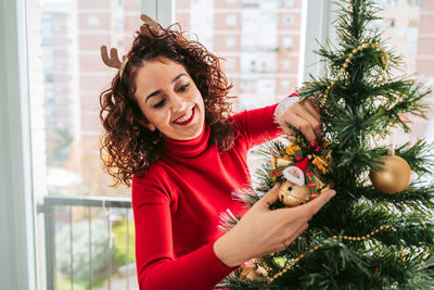 Portrait of happy young woman with christmas tree at home