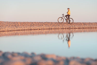 Man riding bicycle by lake against sky