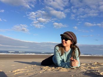 Woman smiling while lying at beach against sky