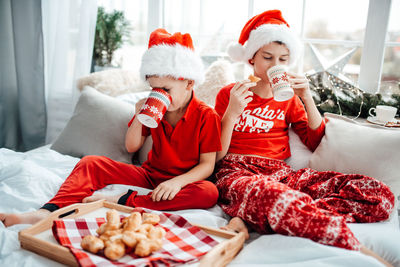 Cute kids drinking hot chocolate while sitting on bed at home