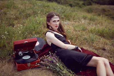 Young woman lies in nature in a black dress next to an old gramophone and listens to music