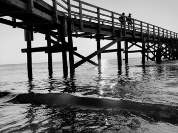 Low angle view of people walking on pier over sea against sky