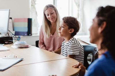 Mother and son consulting doctor with female nurse at desk in clinic