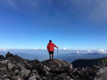 Rear view of man standing on rock against blue sky