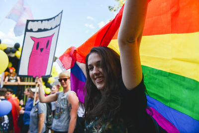 Happy young woman holding colorful flags against sky