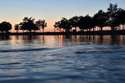 Silhouette trees by swimming pool against sky during sunset