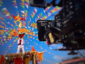 Video camera photographing man standing on thatched roof against blue sky