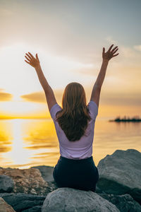 Rear view of woman doing yoga at beach against sky during sunset