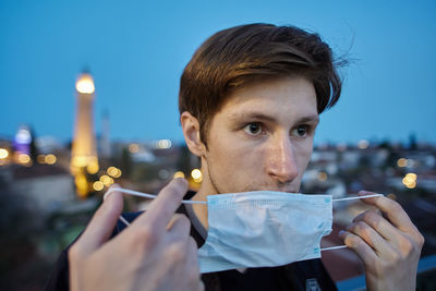 Portrait of young man holding illuminated cityscape against sky