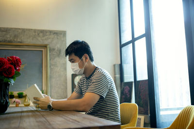 Man wearing mask reading book at home