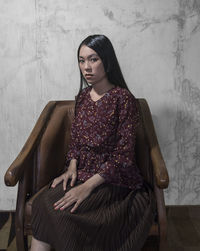 Portrait of young woman sitting on seat against wall