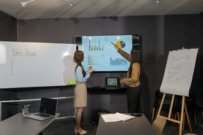 Rear view of woman using mobile phone while standing in office