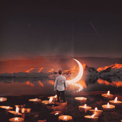 Digital composite image of man standing in tea light candle against lake and moon at night