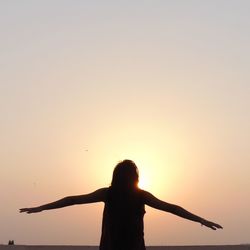 Silhouette woman with arms outstretched against sky during sunset