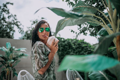 Young woman wearing sunglasses standing against plants