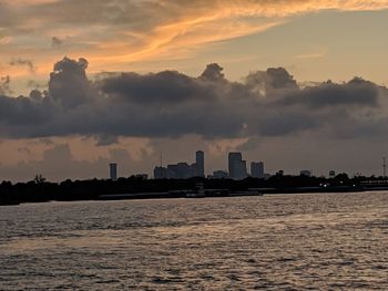 Silhouette buildings by sea against sky during sunset
