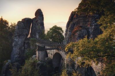 Arch bridge and rock formations against sky during sunset