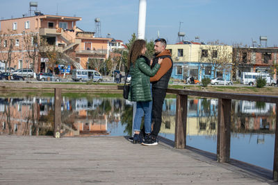 Side view of couple romancing while standing on pier by lake
