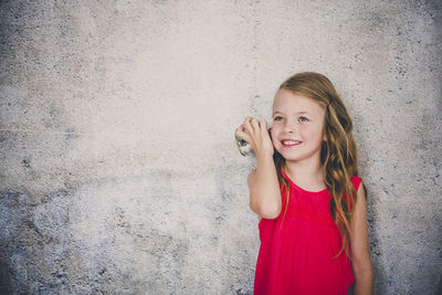 Cute smiling girl playing with tin can phone while standing against wall