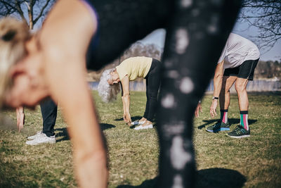 Senior friends learning from female coach while bending on field during sports training