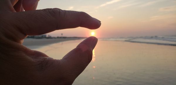 Midsection of man at beach against sky during sunset