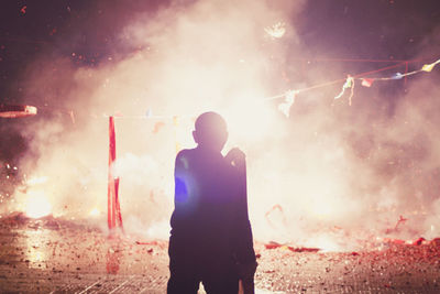 Rear view of man standing by fireworks on street at night