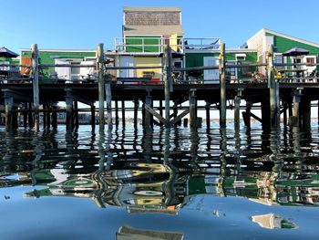 Pier on lake by buildings against clear blue sky