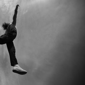 Low angle view of woman jumping against sky