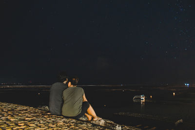 Rear view of couple sitting at park against sky at night